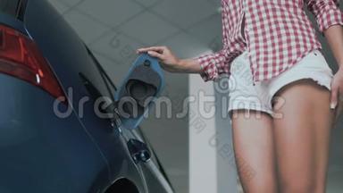 有着苗条黝黑的腿的女人把充电放在电动汽车的电源插座上